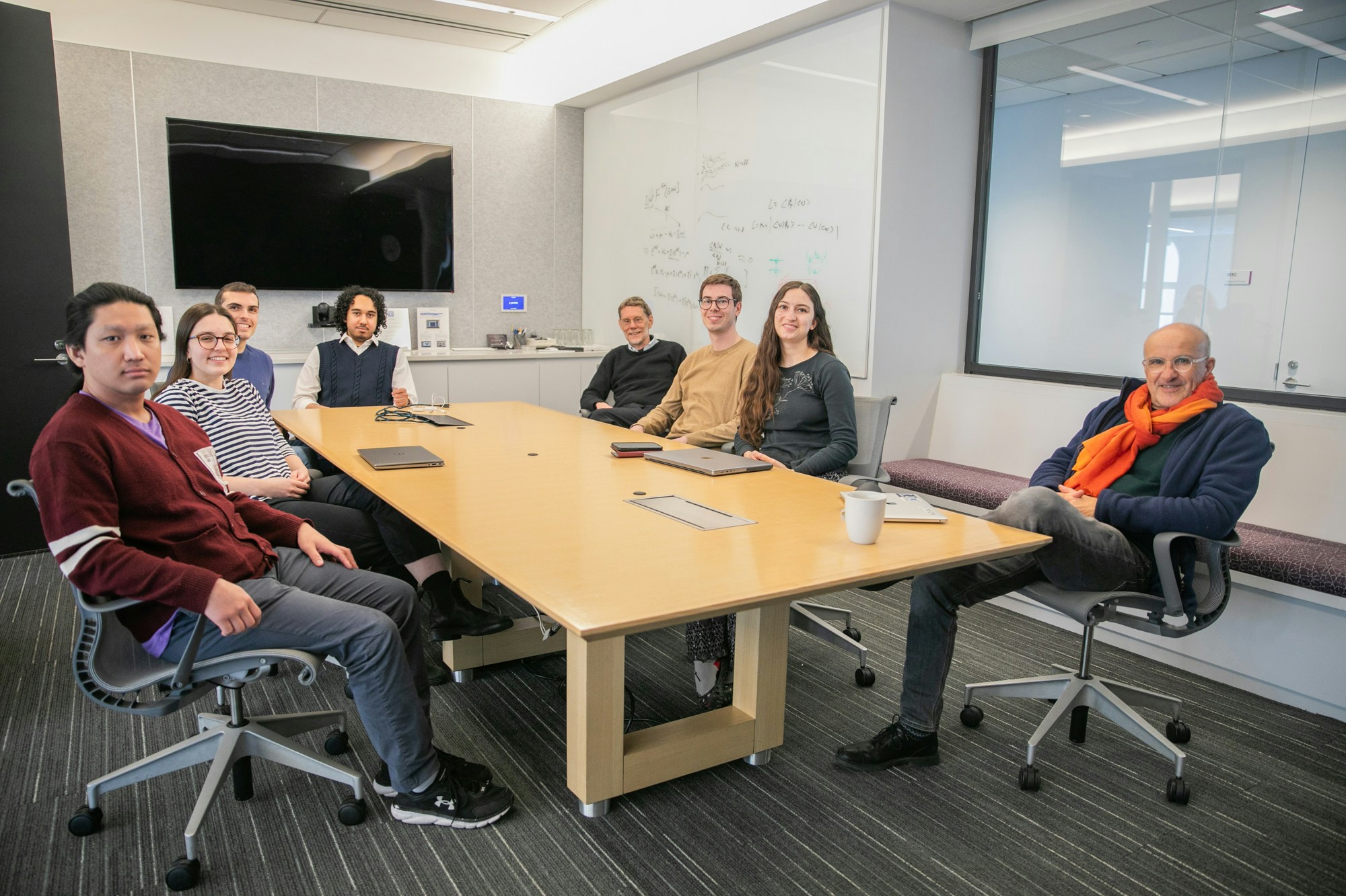 students and scientist sit around a conference table with a tv screen in the background